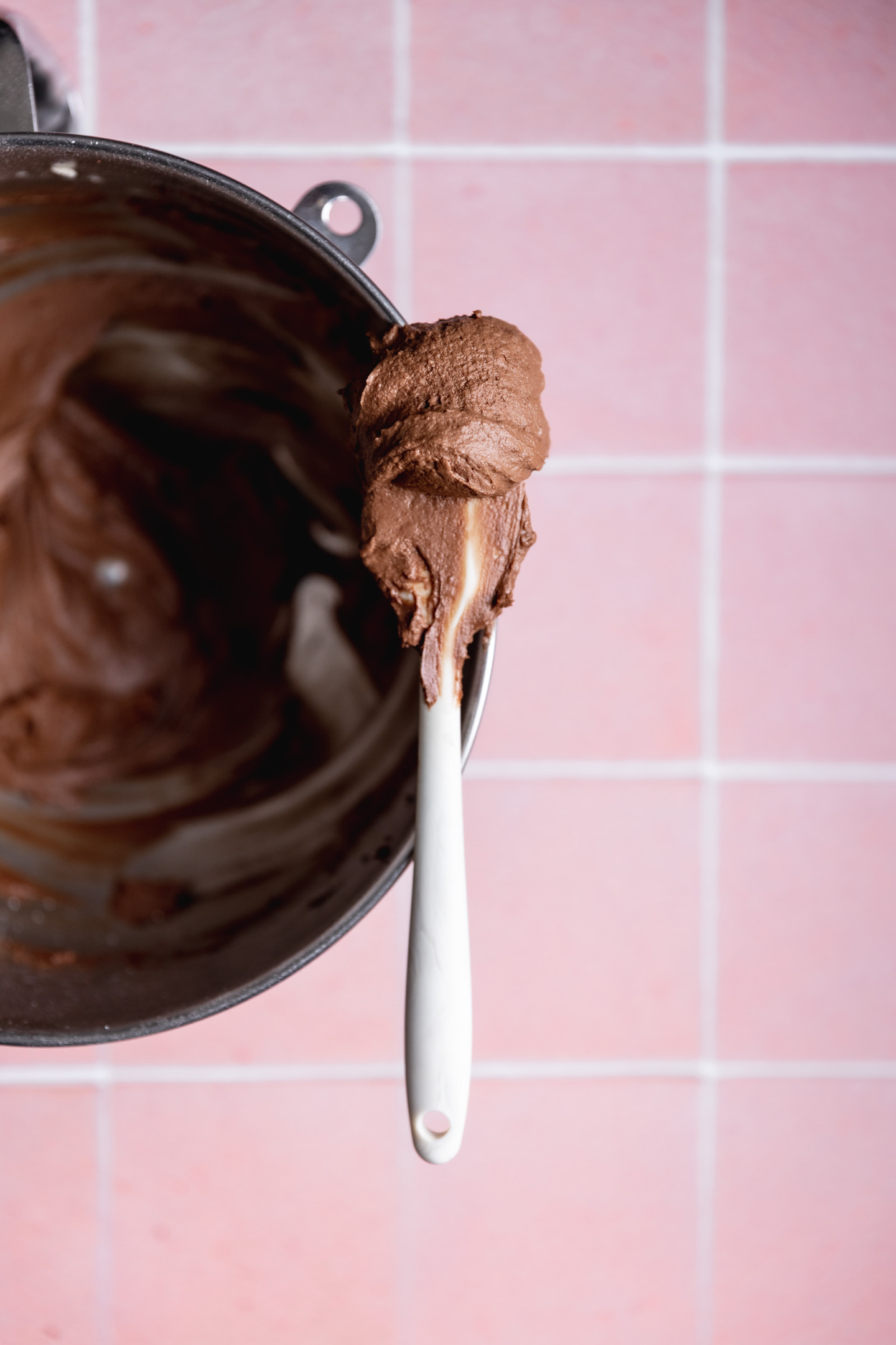 A spatula over a mixing bowl with dairy free chocolate frosting on it.