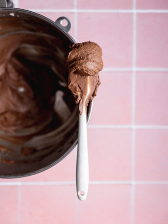 A spatula over a mixing bowl with dairy free chocolate frosting on it.