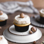 A cookie dough cupcake frosted with cookie dough garnish on an over turned plate.