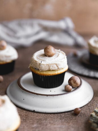 A cookie dough cupcake frosted with cookie dough garnish on an over turned plate.