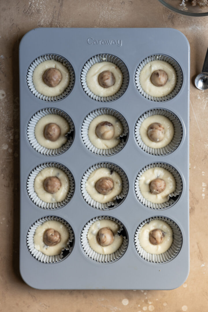 Cookie dough balls on top of cupcake batter in a muffin tin.