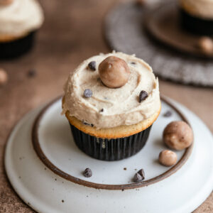 A cookie dough cupcake on an upside down plate on a brown surface.