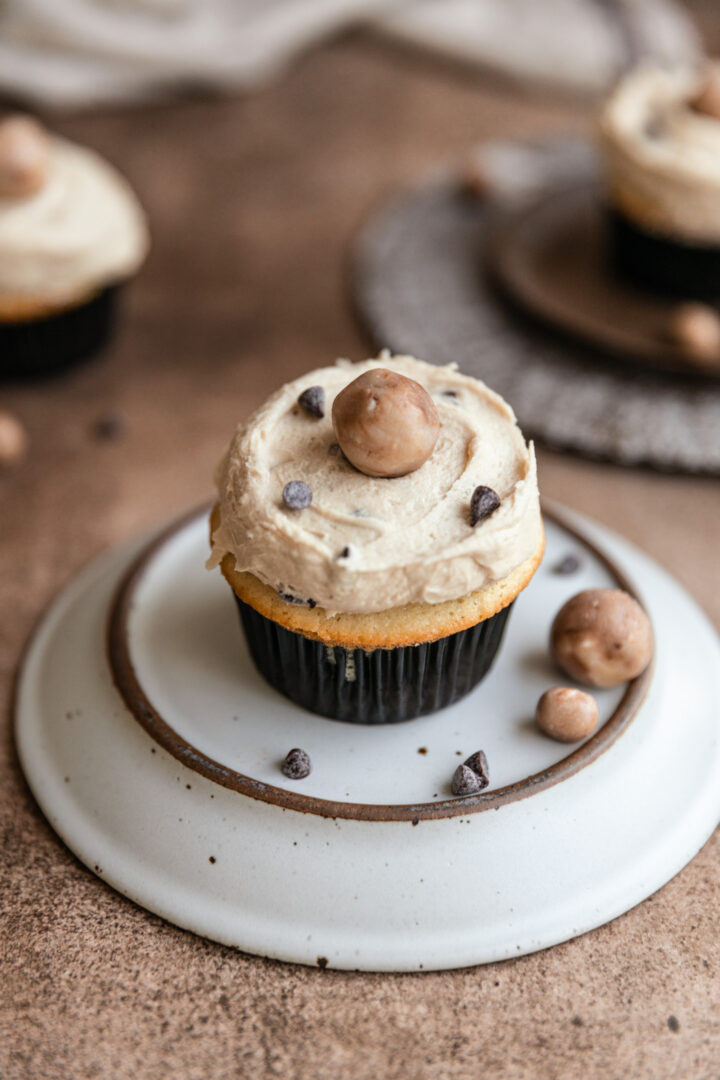 A cookie dough cupcake on an upside down plate on a brown surface.