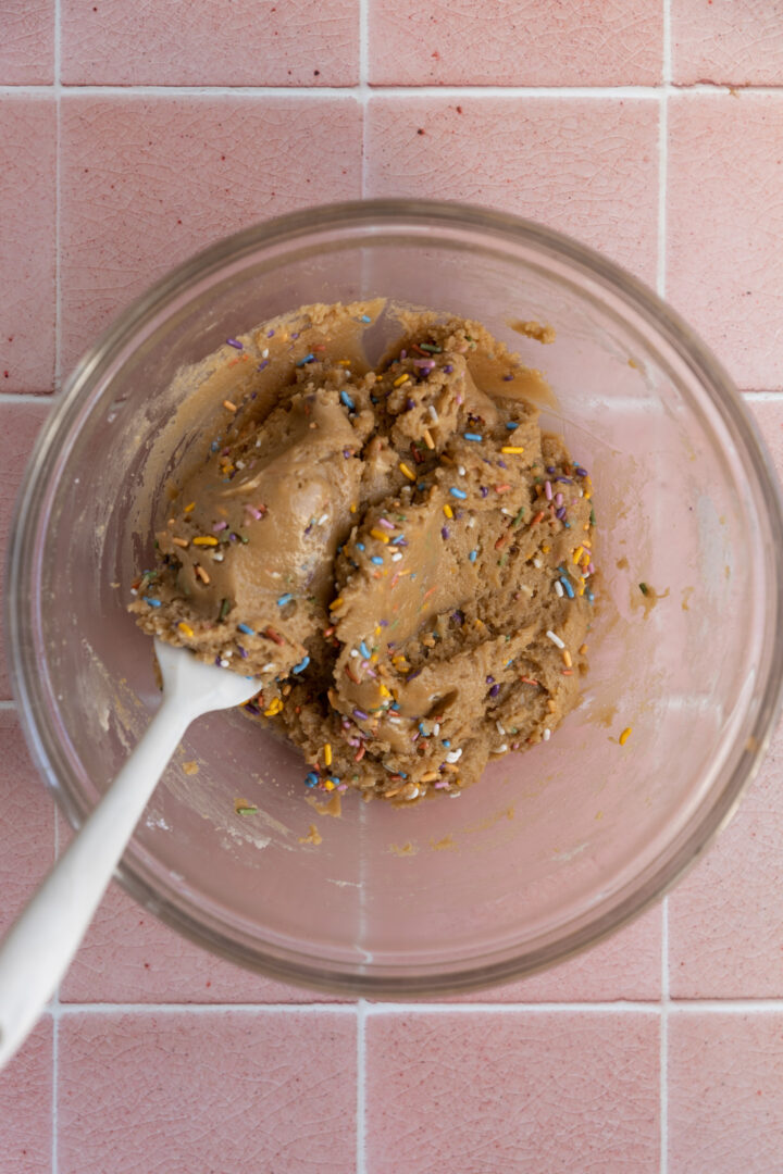 Birthday cake cookie batter in a glass bowl.