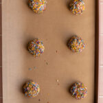 Birthday cake cookie dough balls lined on a baking sheet.