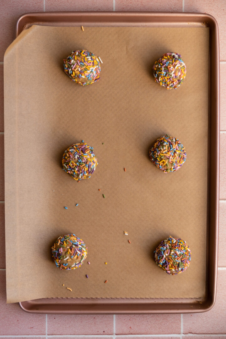 Birthday cake cookie dough balls lined on a baking sheet.
