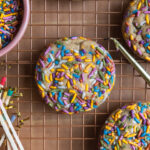 A colorful sprinkle cookie on a cooling rack next to candles and matches.