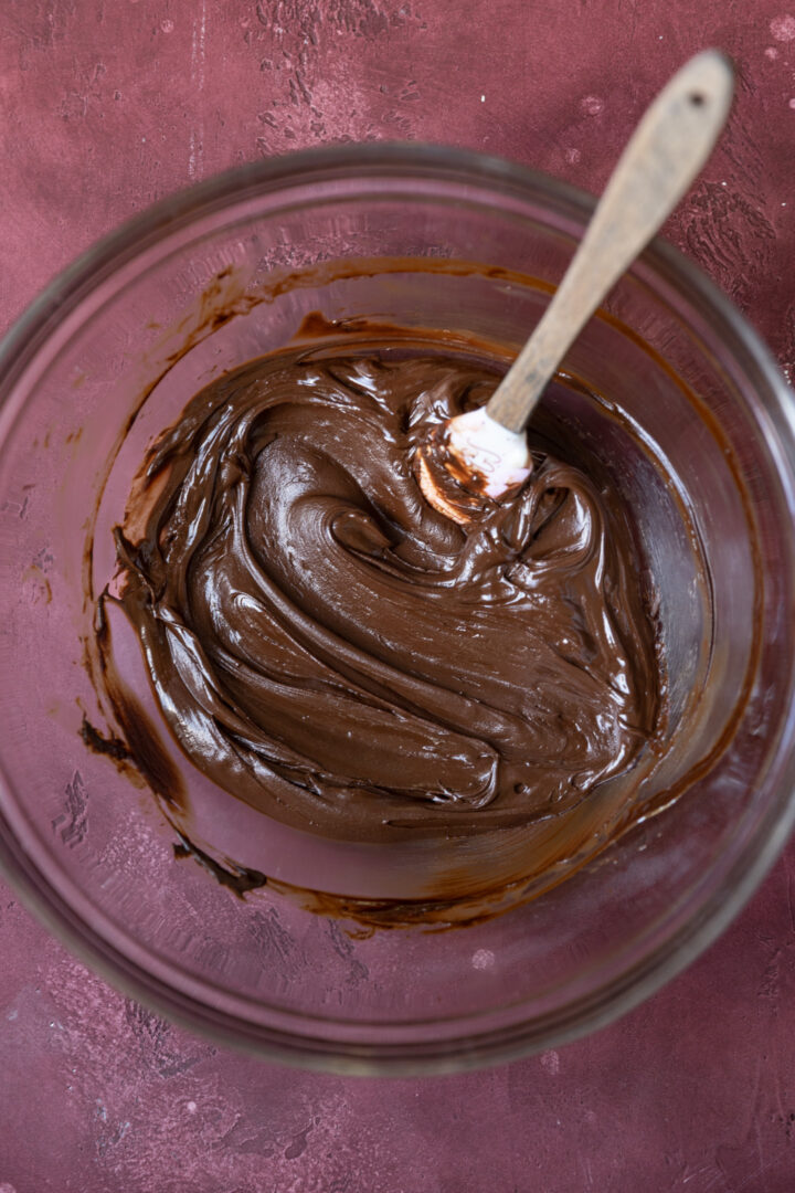 Melted chocolate and butter combined with egg yolks in a glass bowl.