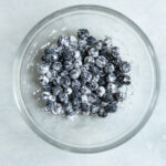 Fresh blueberries coated in flour in a glass bowl.