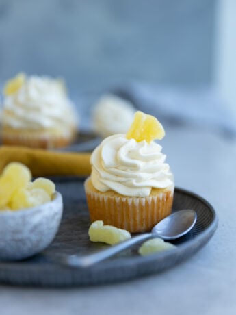 A pineapple cupcake garnished with candied pineapple on a blue plate next to a resting spoon.