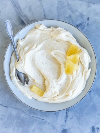Pineapple frosting in a white bowl on a blue surface.