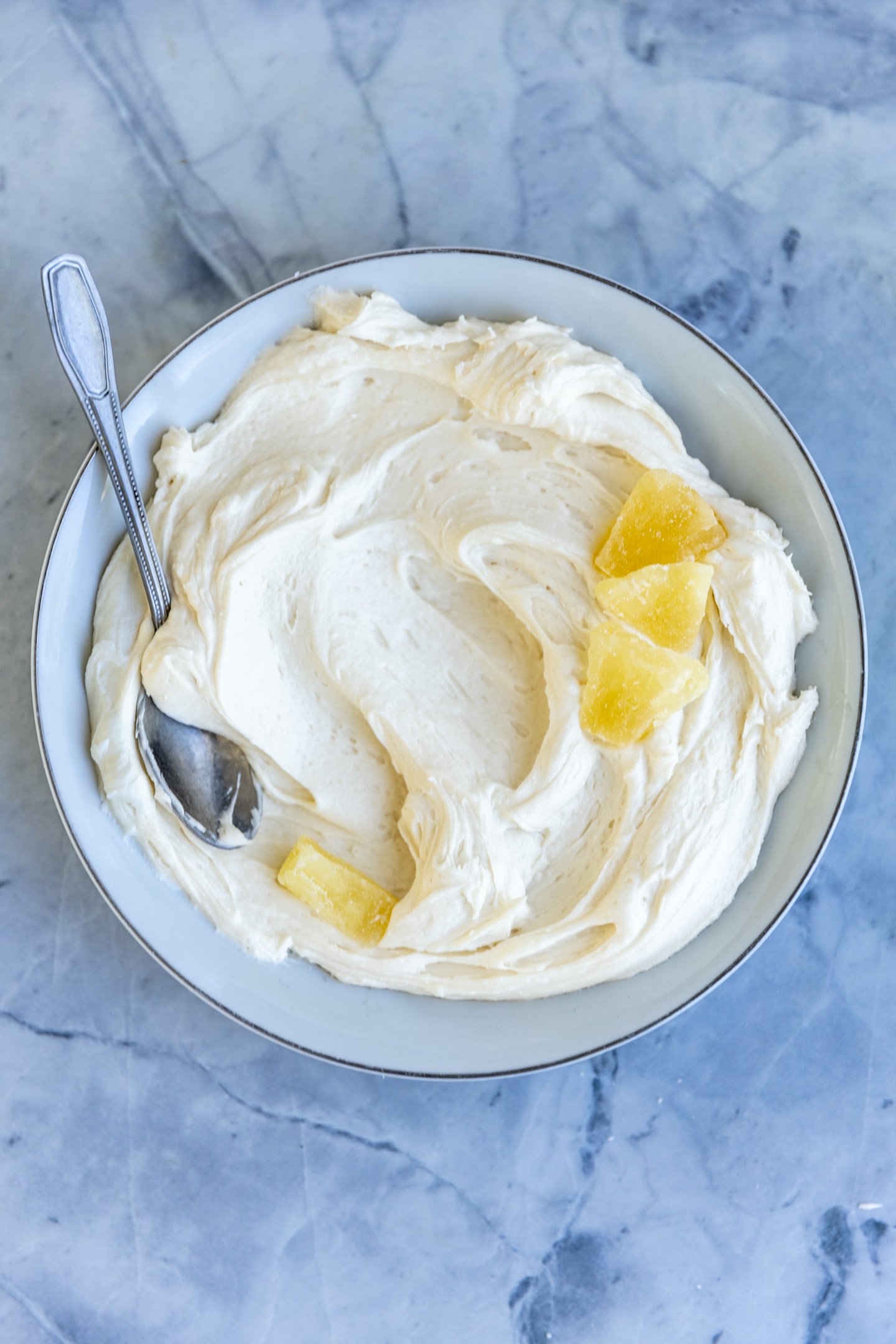 Pineapple frosting in a white bowl on a blue surface.
