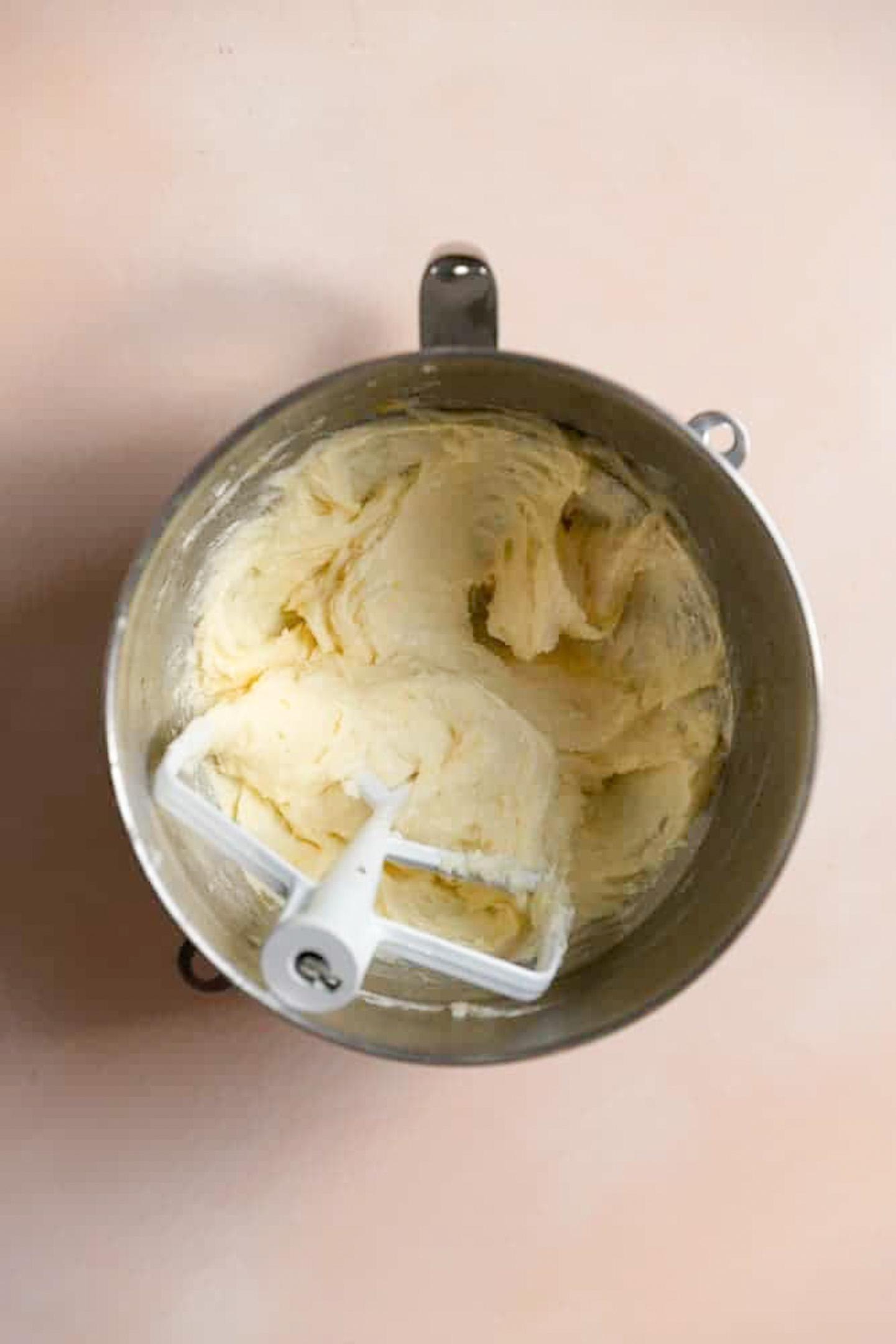 A mixture or butter, sugar, and eggs in a mixing bowl with a paddle attachment.