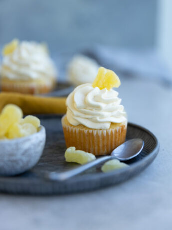 A pineapple cupcake garnished with candied pineapple on a blue plate next to a resting spoon.