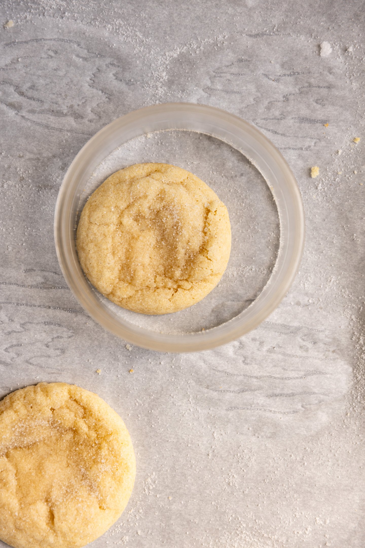 A cookie on a piece of parchment paper with a larger cookie cutter around it. 