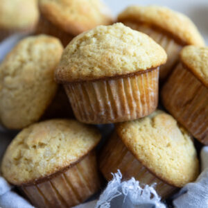 Muffins on top of each other in a bowl lined with a blue linen.