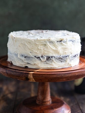 A Guinness chocolate cake with white frosting on a wooden cake stand.