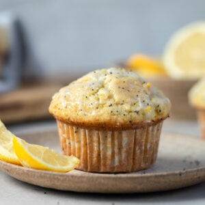 A lemon poppy seed muffin next to a lemon on a plate.
