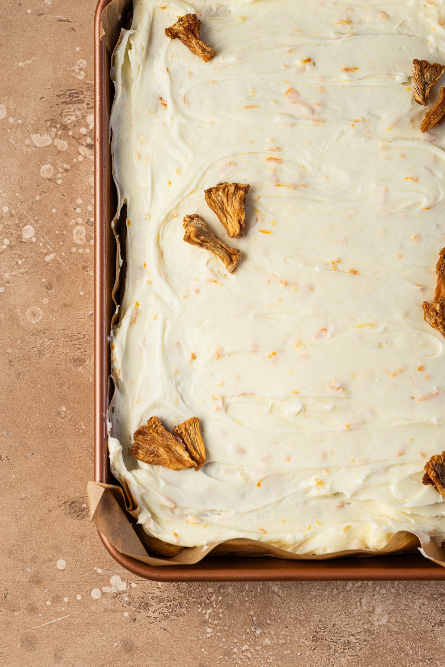 A sheet cake topped with cream cheese frosting and garnished with dried pineapple. 