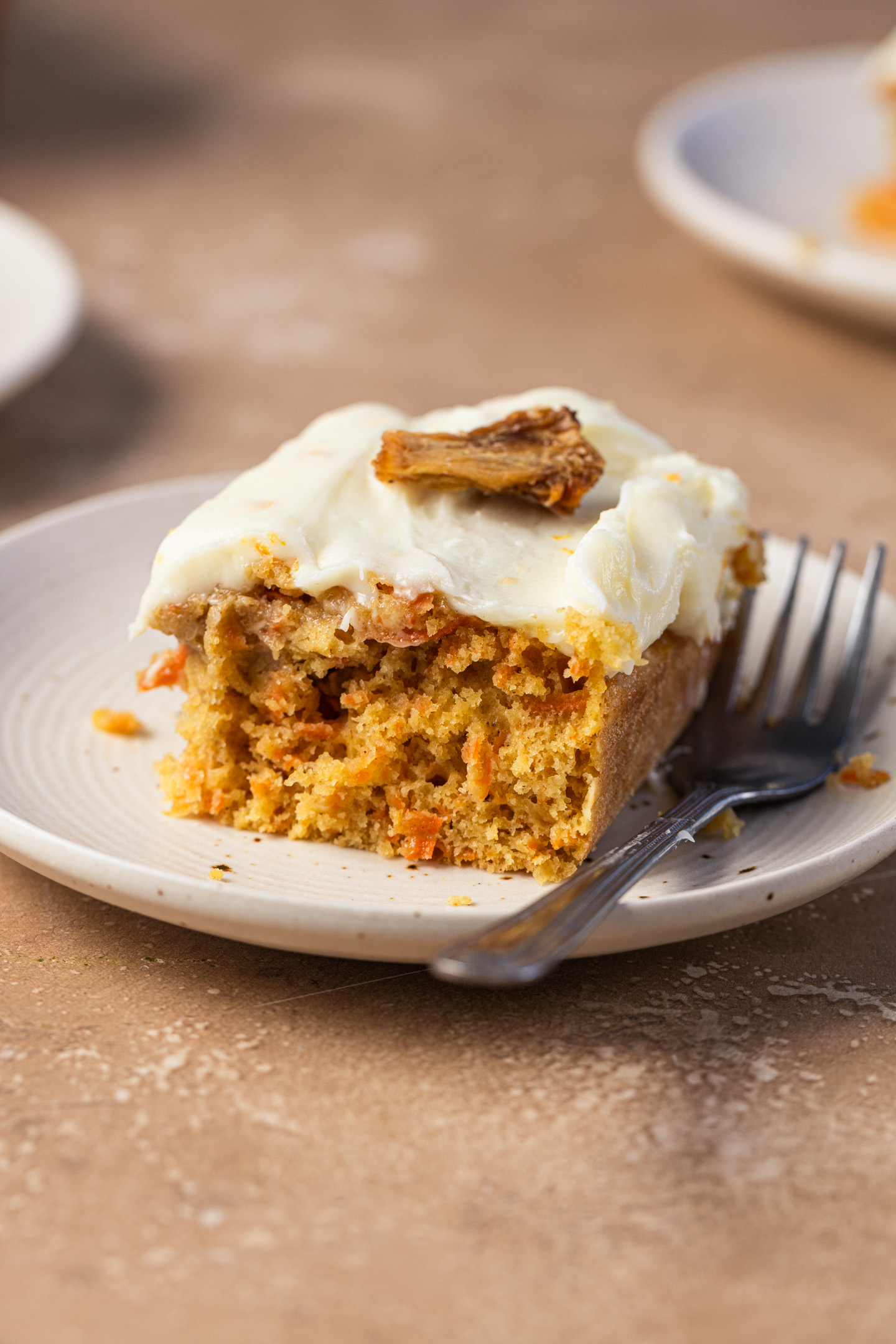 A piece of a carrot pineapple cake on a small plate next to a fork.