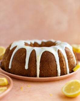 Lemon bundt cake with a white glaze on a pink plate and surface.