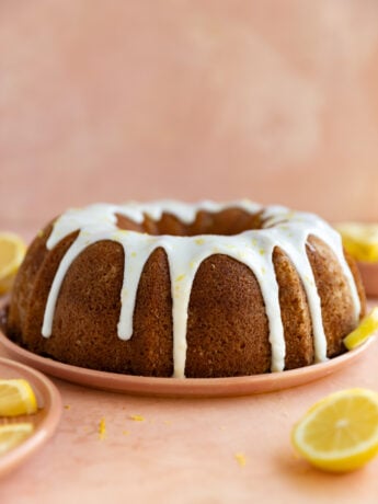 Lemon bundt cake with a white glaze on a pink plate and surface.