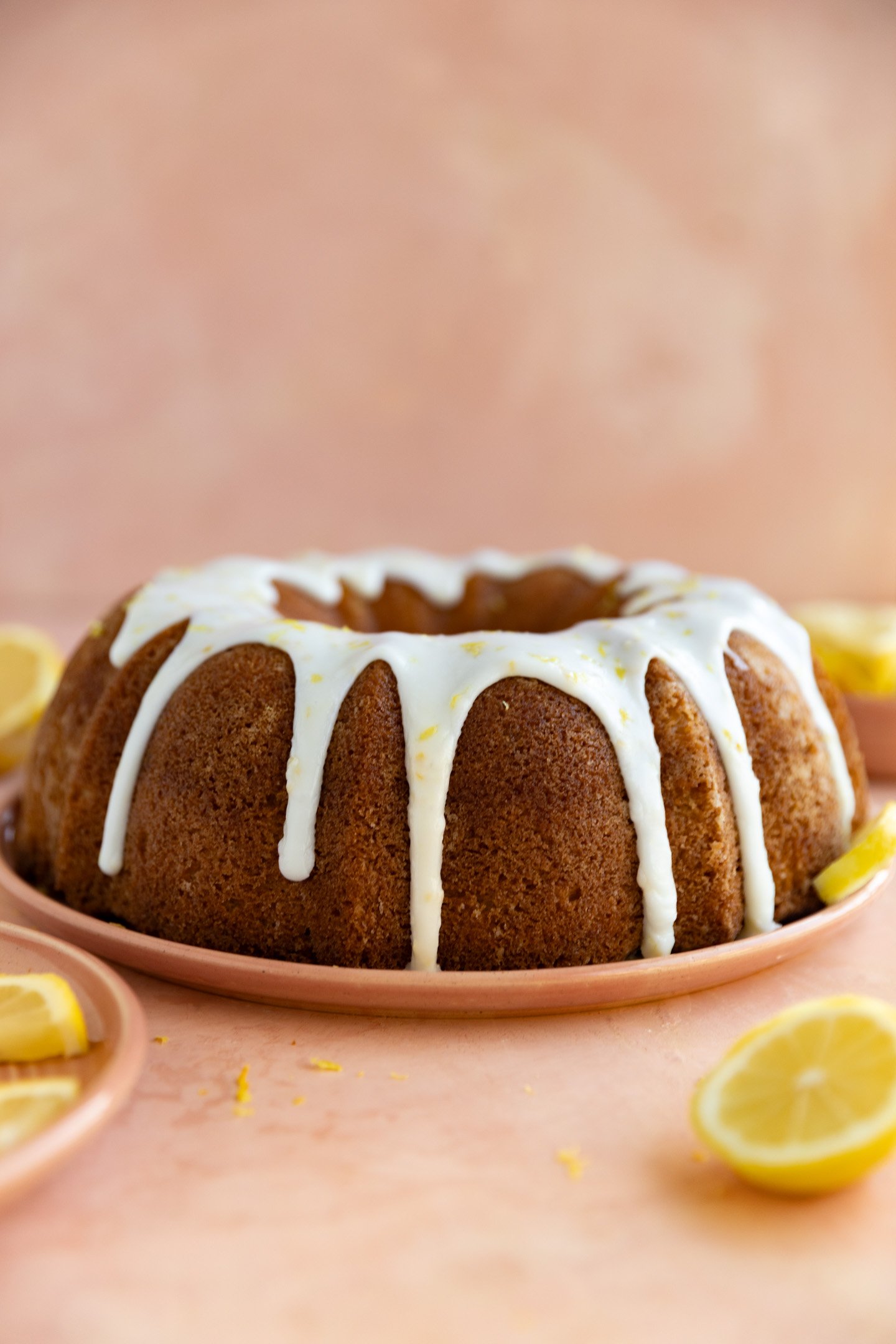 Lemon bundt cake with a white glaze on a pink plate and surface.