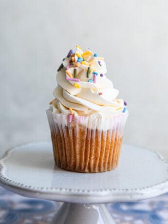 A vanilla cupcake piped with swiss meringue buttercream and colorful sprinkles.
