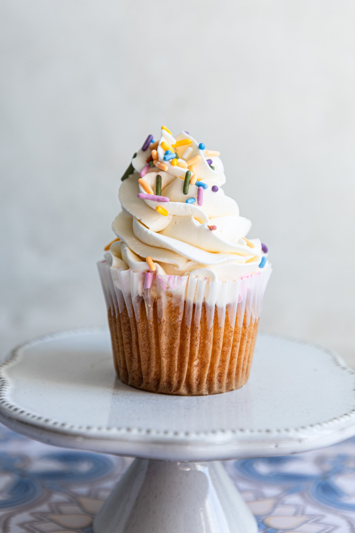A vanilla cupcake piped with swiss meringue buttercream and colorful sprinkles.