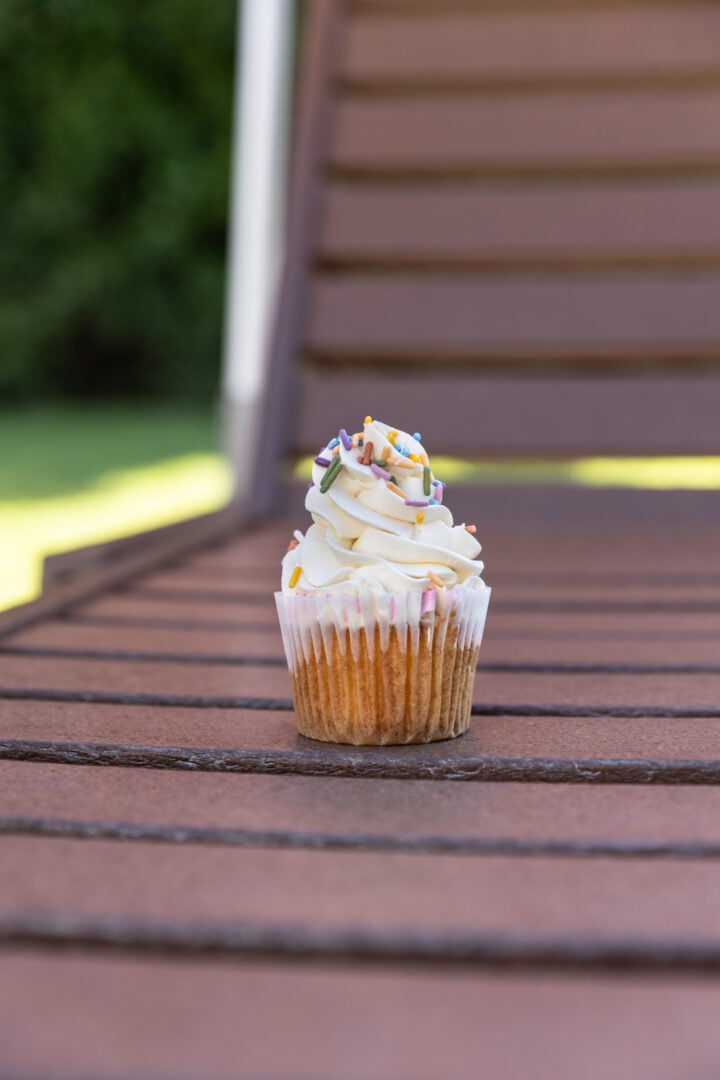 A vanilla cupcake with sprinkles on a chair. 