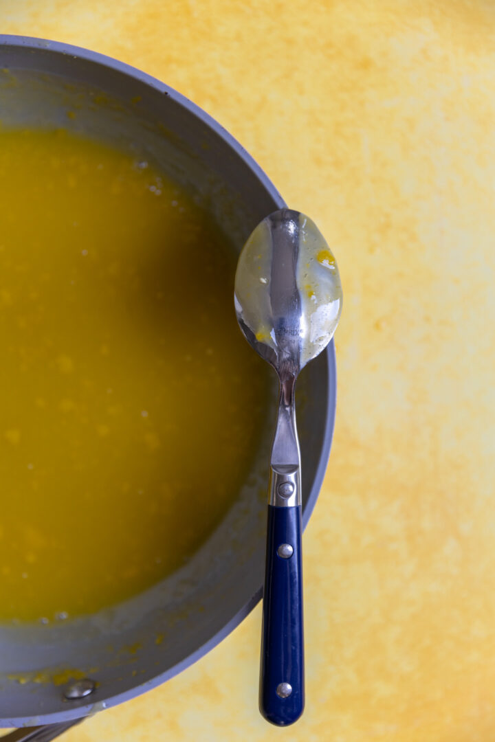 A spoon resting over a pan of lemon curd. 