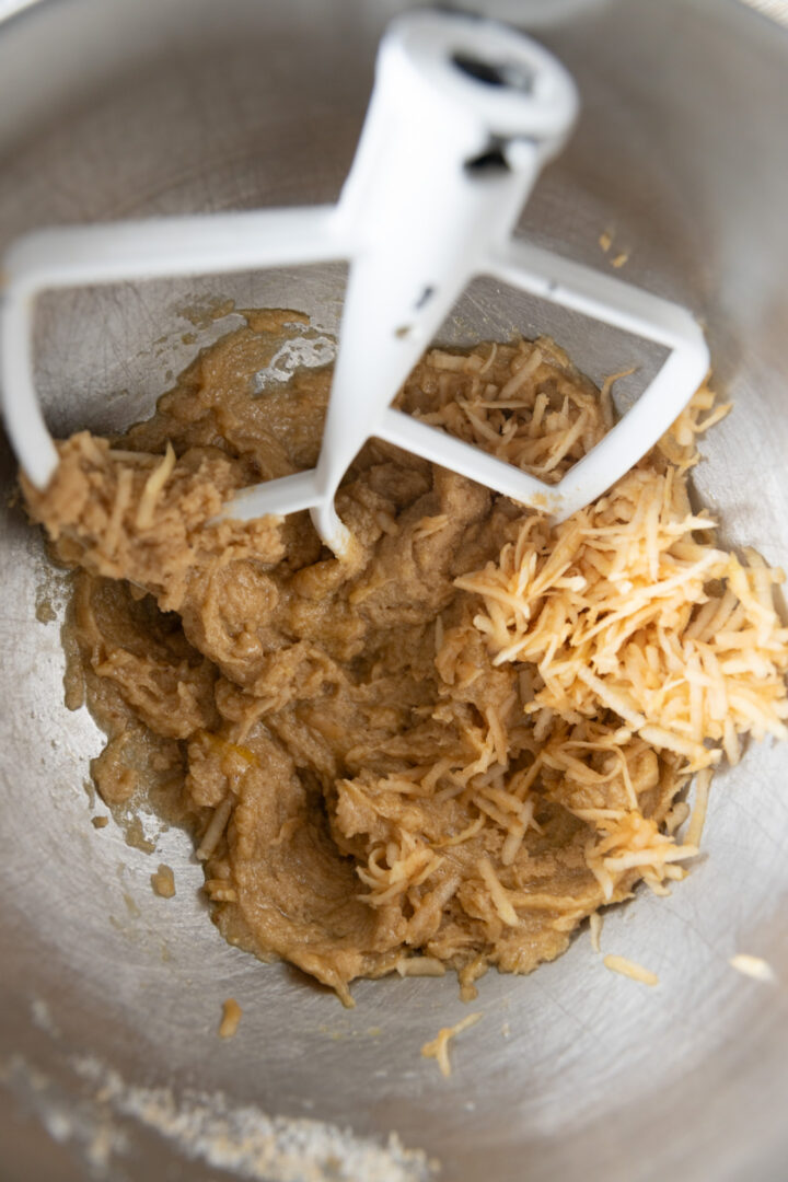 Grated apple added to creamed butter and sugar in a mixing bowl.