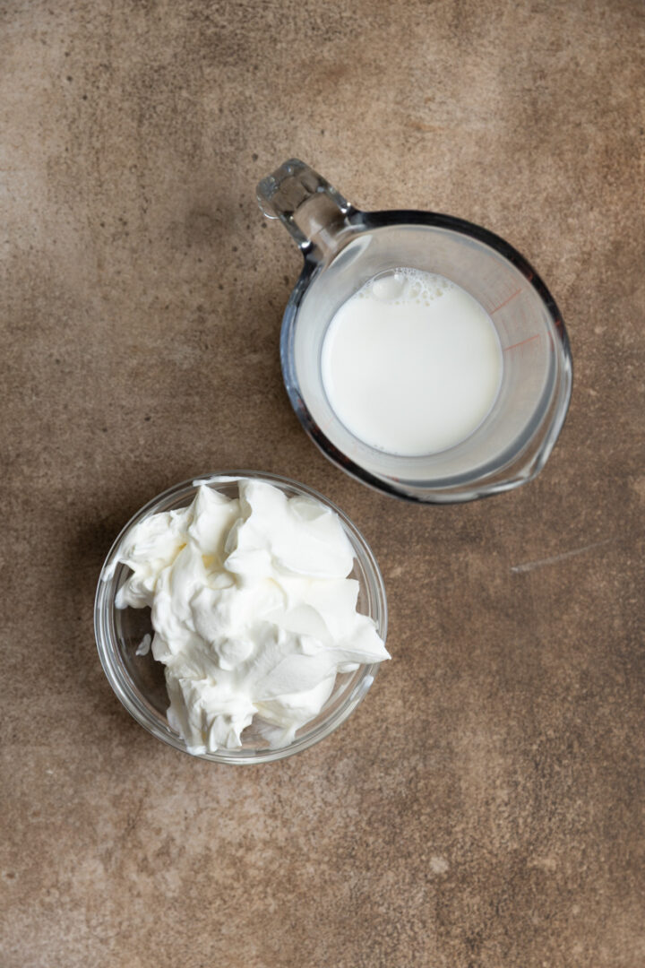 Sour cream and milk measured out on a brown board.