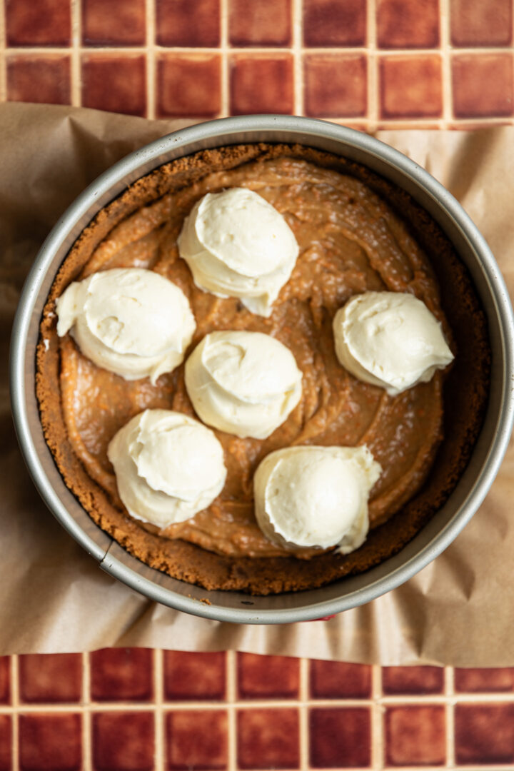 Cheesecake batter scooped on top of carrot cake batter.