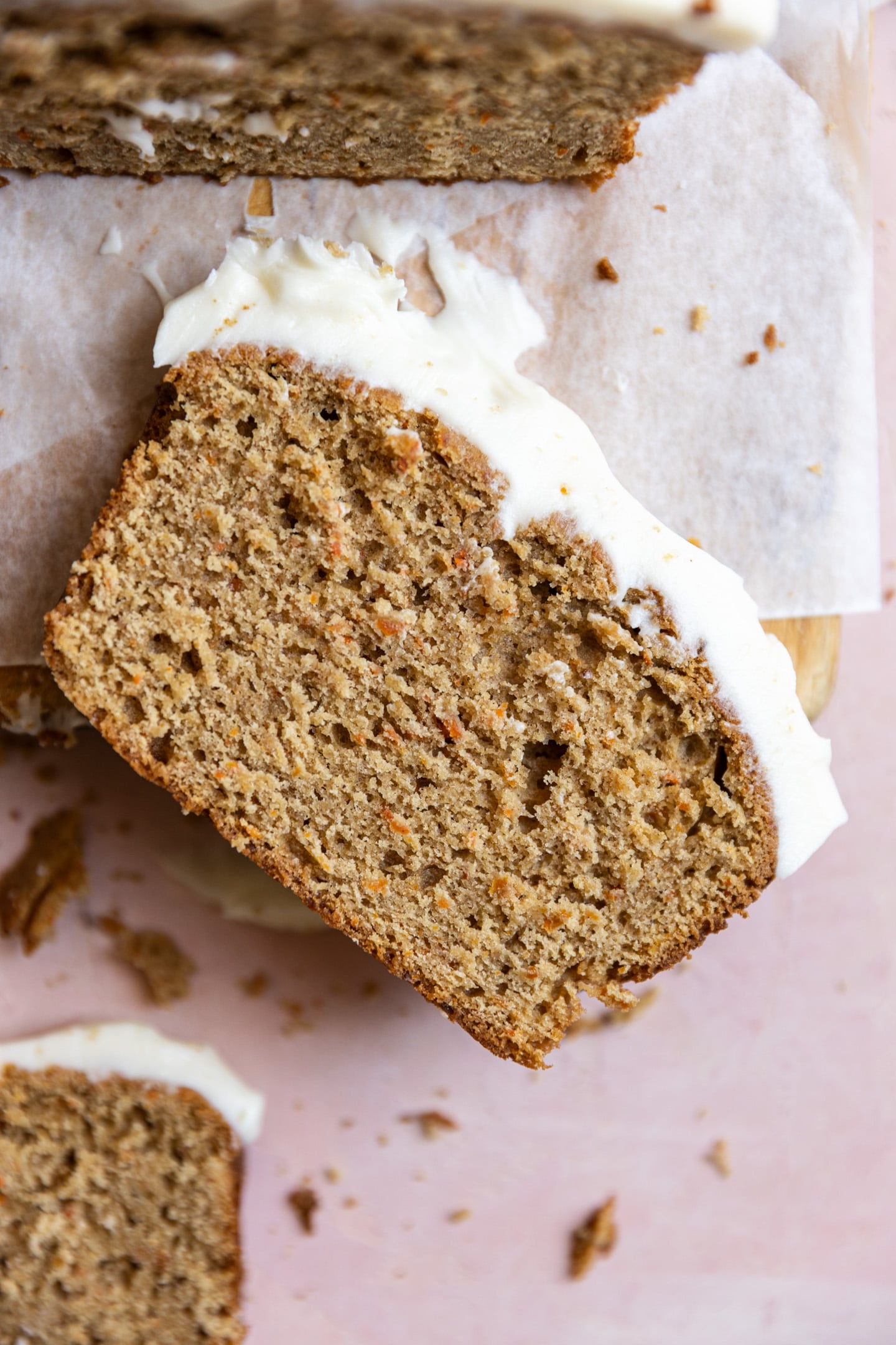 A slice of carrot cake loaf on a wooden cutting board.