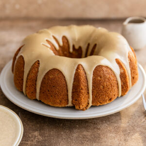 A brown sugar cake with brown sugar glaze on a white plate on a brown surface.