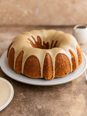 A brown sugar cake with brown sugar glaze on a white plate on a brown surface.