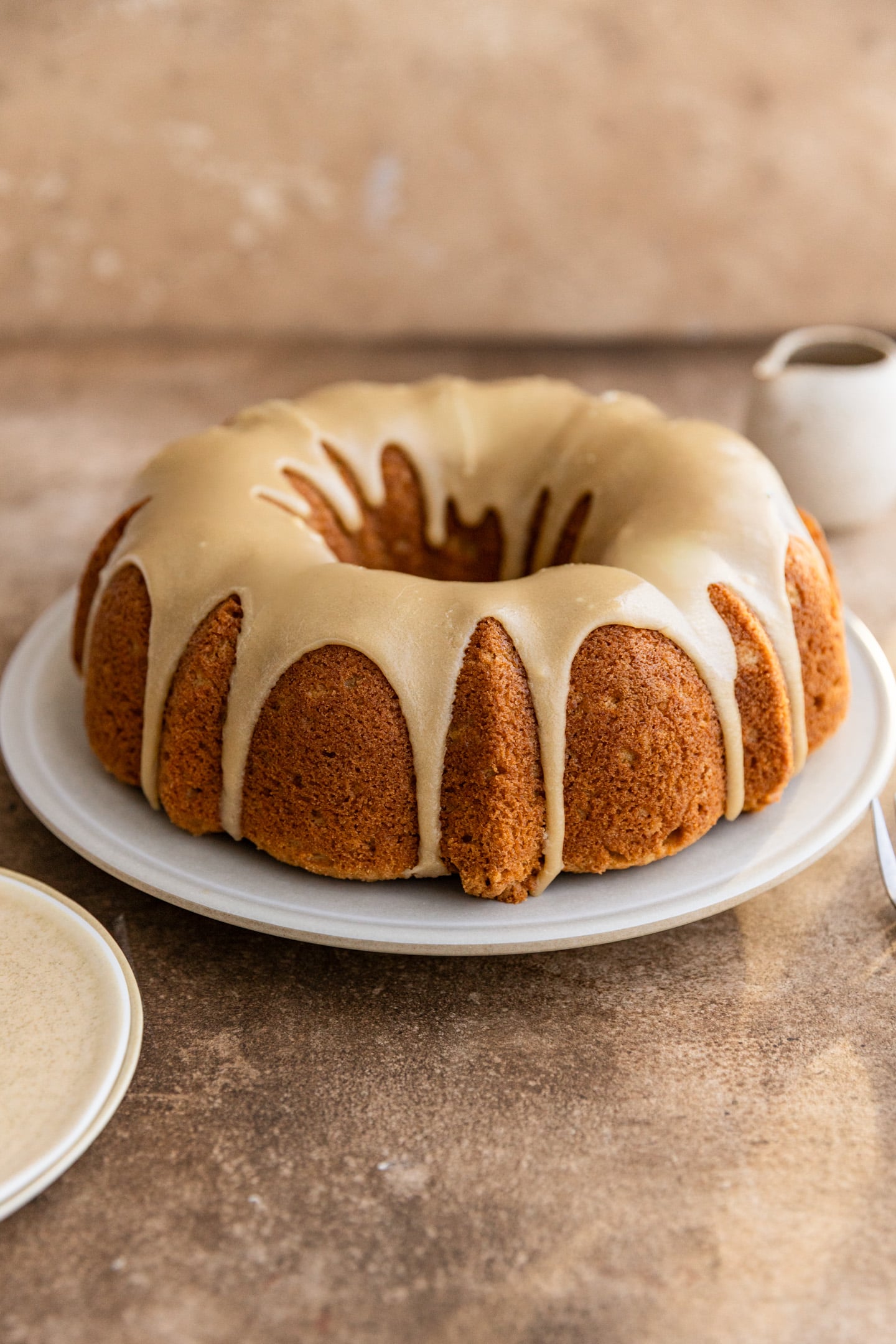 A brown sugar cake with brown sugar glaze on a white plate on a brown surface.
