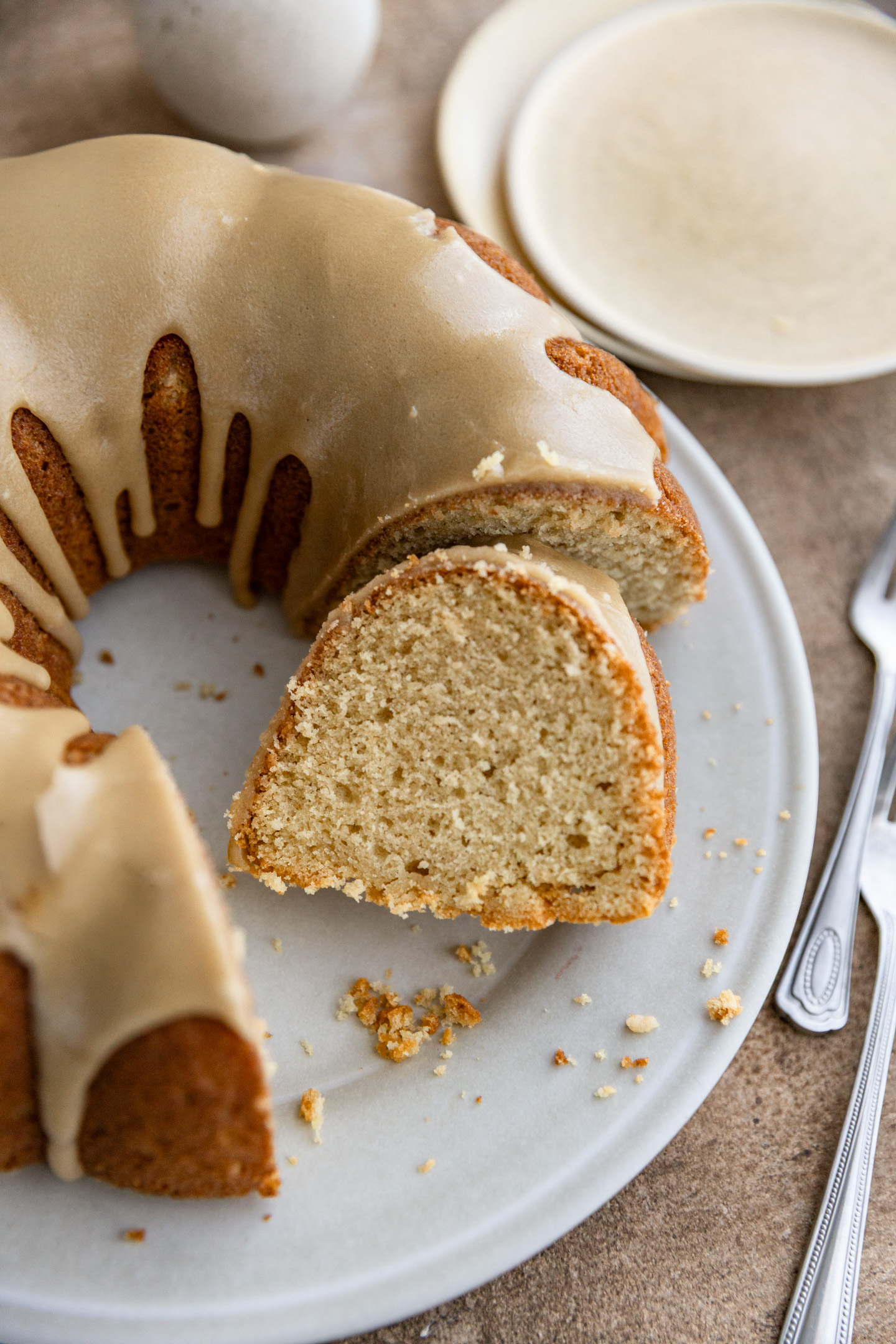 A slice of a brown sugar cake cut out and lying next to the full cake on a white plate.