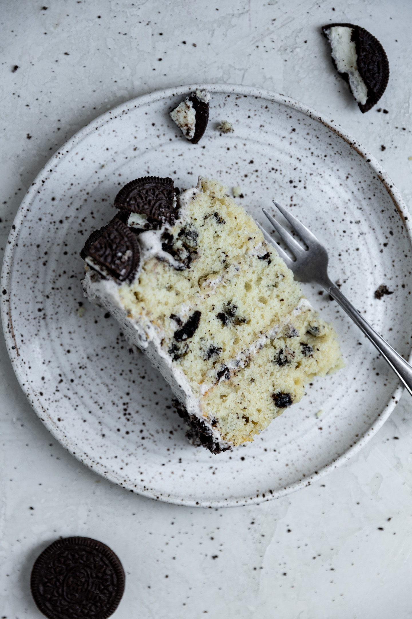 A slice of cookies and cream cake on a white speckled plate.