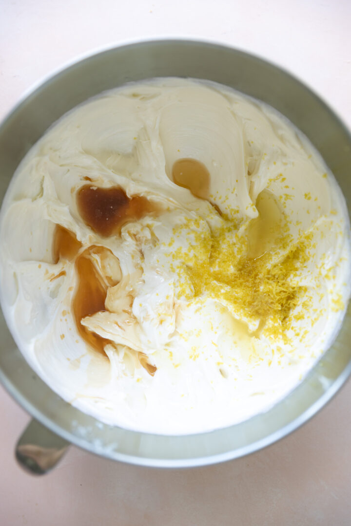 Lemon juice, zest and vanilla extract on top of a cream cheese and sugar mixture in a bowl.