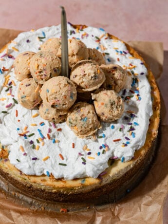 A birthday cake cheesecake topped with whipped cream and edible sugar cookie dough.