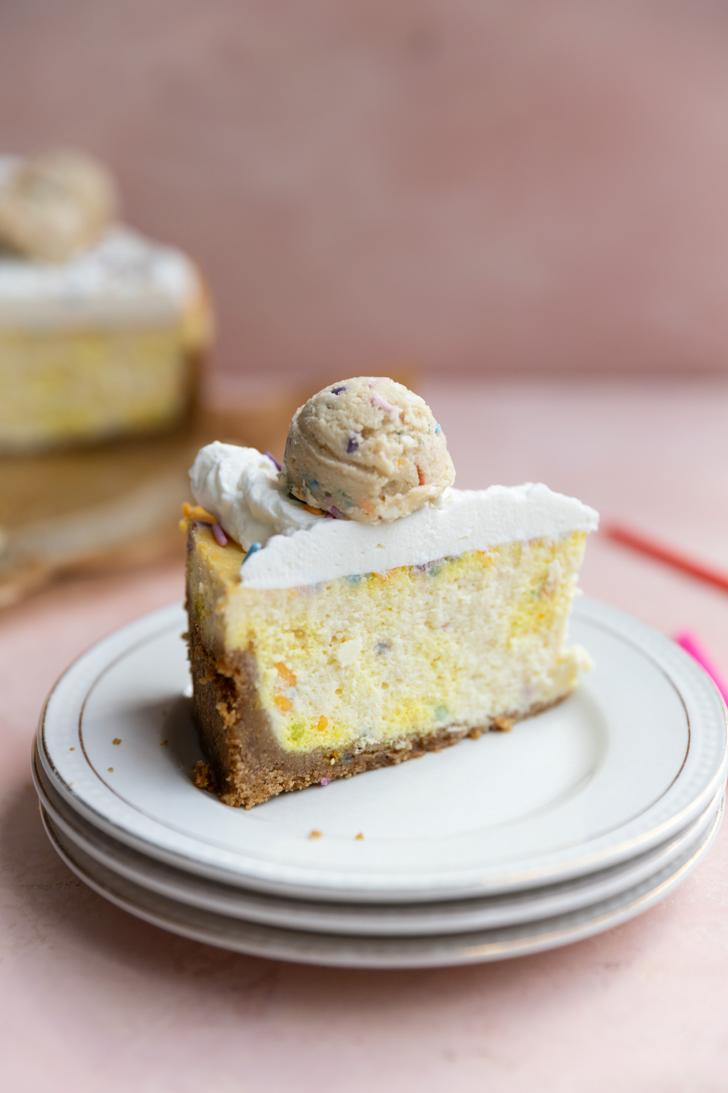 A slice of birthday cake cheesecake on stacked plates.