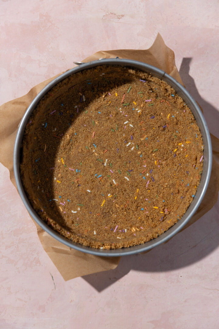 Graham cracker crust with sprinkles pressed into a springform pan.