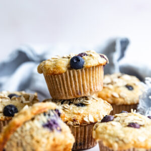 Banana Blueberry Oat Muffins stacked on each other on a white surface.
