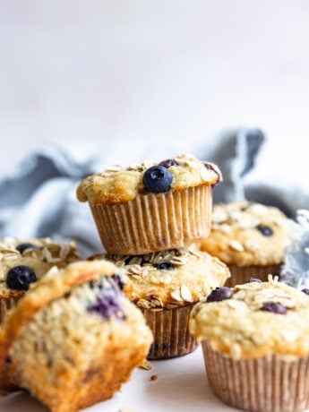 Banana Blueberry Oat Muffins stacked on each other on a white surface.