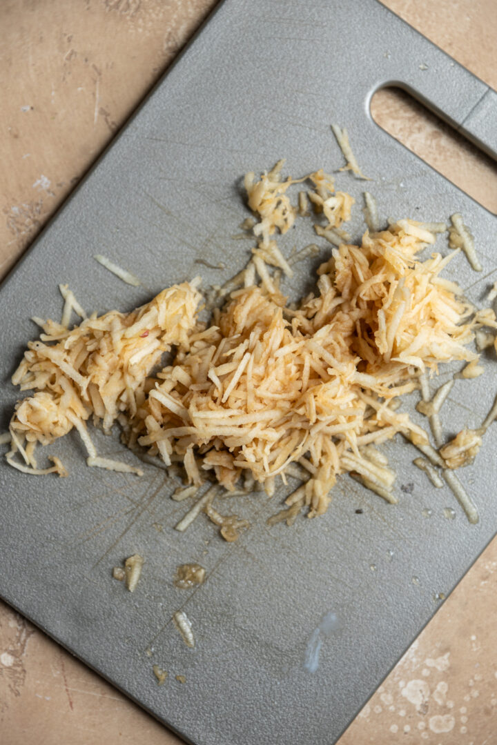 Grated apple on a gray cutting board.