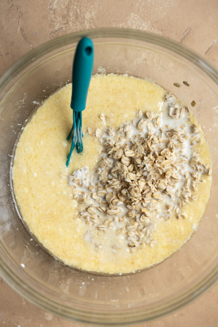 Wet ingredients added to soaked oats in a mixing bowl.