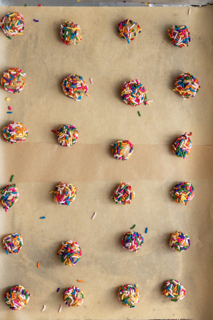 Mini sprinkle sugar cookie dough balls lined on a parchment lined baking sheet.