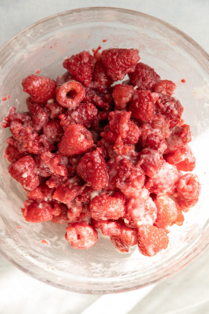 Fresh raspberries tossed with flour and lemon juice in a glass bowl.